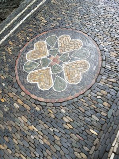 Tan hearts and chocolate tears surround a four leaf clover inside of a circle of red and a circle of black rocks. 