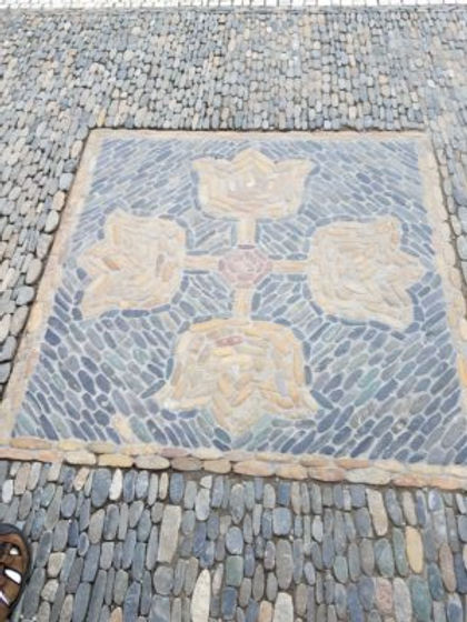 In front of the florist shop, a foursided design of tulips on a cross. The tulips are light pink rocks on a diagonal background of small dark gray rocks in a rectangle./Richen