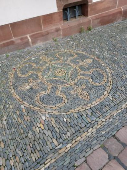 Red bricks line the bottom of the window. The river rock design is a circle of tan inside of gray. The nearby vent from the basement has a little plant design in the grill./Richen
