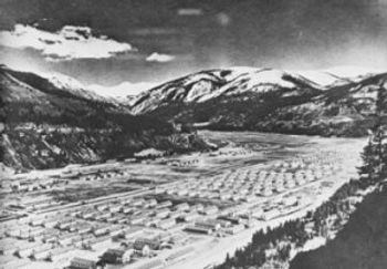 Large valley filled with living quarters for troops and surrounded by high Rocky Mountains.