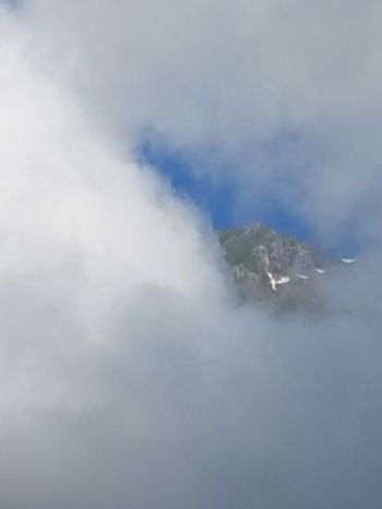 Behind thick clouds, you can barely see the dark rock of a mountain.