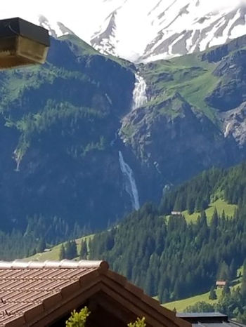 Green and rocky hills carved in two by a long waterfall coming from the glaciated moutains above the towns.
