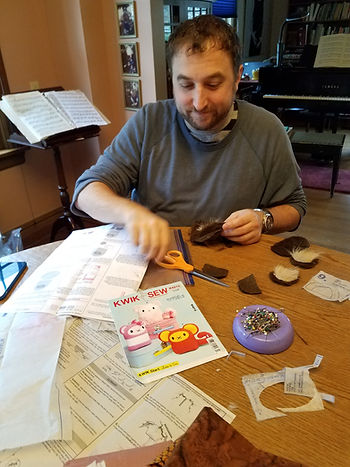 At the dining table, Owyn is cutting out parts. there is a mess of patterns and pins all over the table.