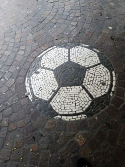 Among the concentric curves of cobblestone, a soccer or futbal sits before the sporting goods stores./Richen