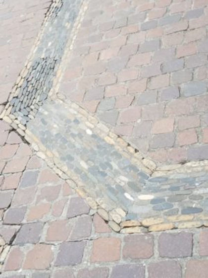 Red cobblestones with a river-rock drain for rain wanter. The drain turns a corner in orderly fashion with small rocks on the inner curve corner and larger ones at the outer edge../Richen